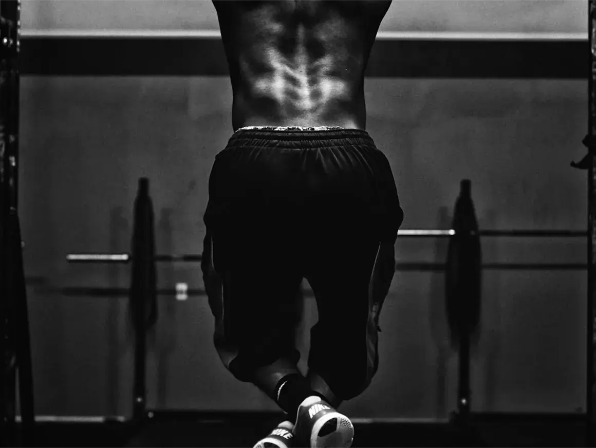 Close-up back view of a person performing a pull-up, highlighting back muscle definition during intense workout
