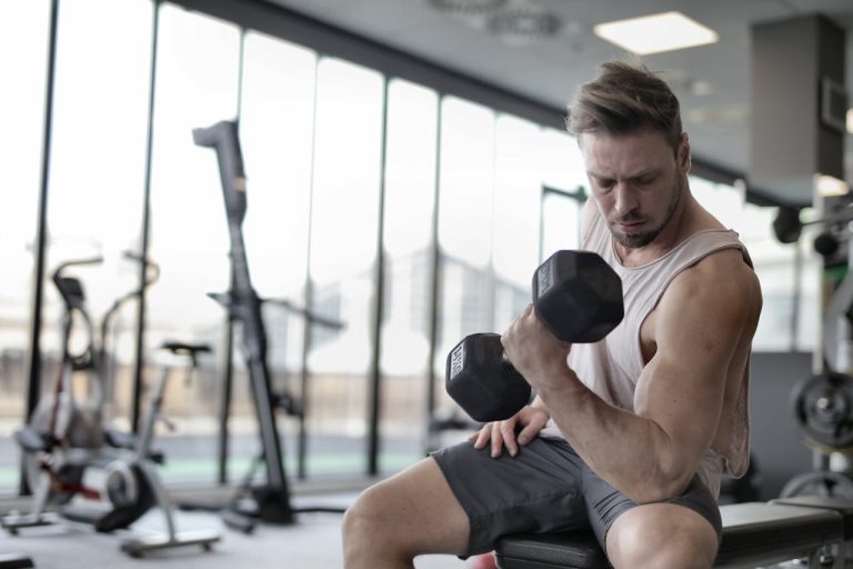 Ein Mann, der auf einer Fitnessbank sitzt und im Sitzen Bizeps-Curls mit Hanteln ausführt